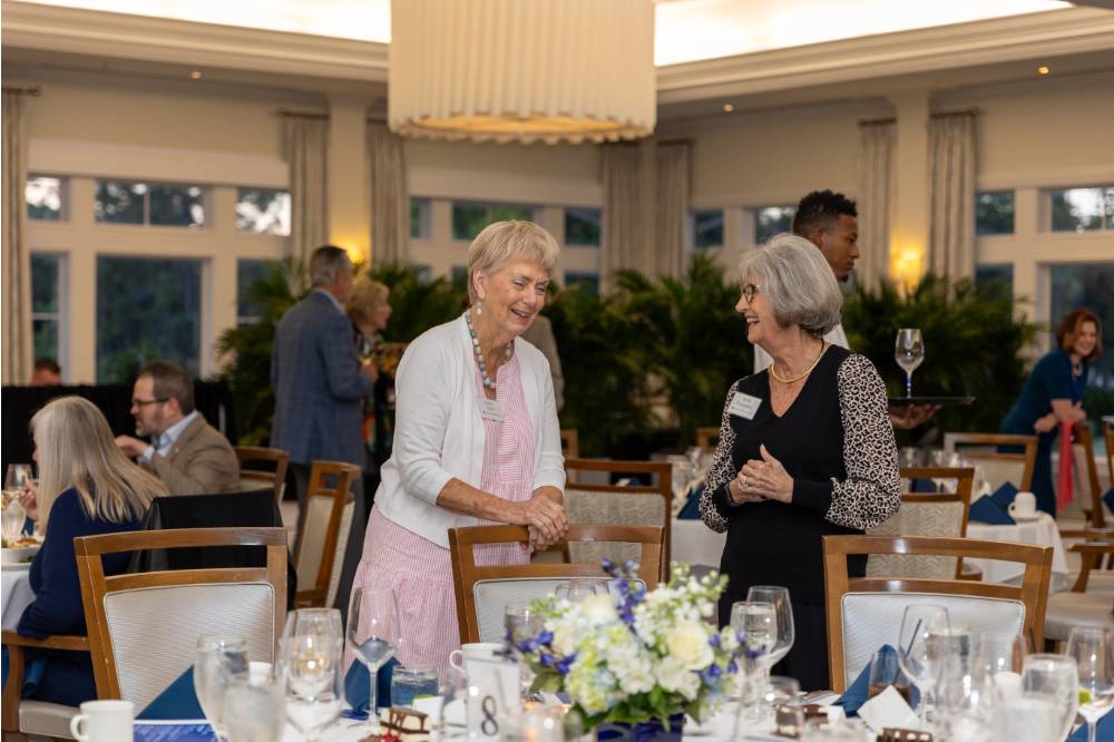 Lydia Tobian and Anita Christopher chatting while standing by their table